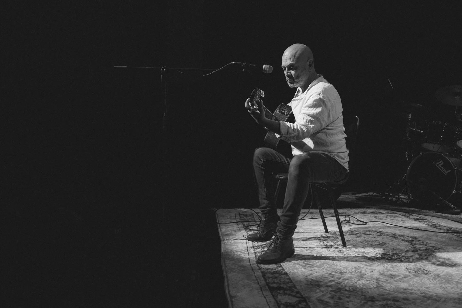 Alexis Venegas sentado en un taburete, solo en el escenario, con su guitarra.